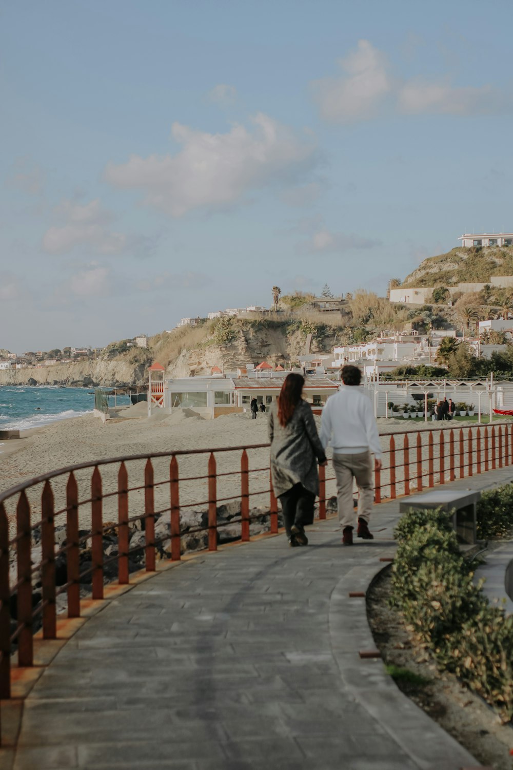 a man and a woman walking down a sidewalk next to the ocean