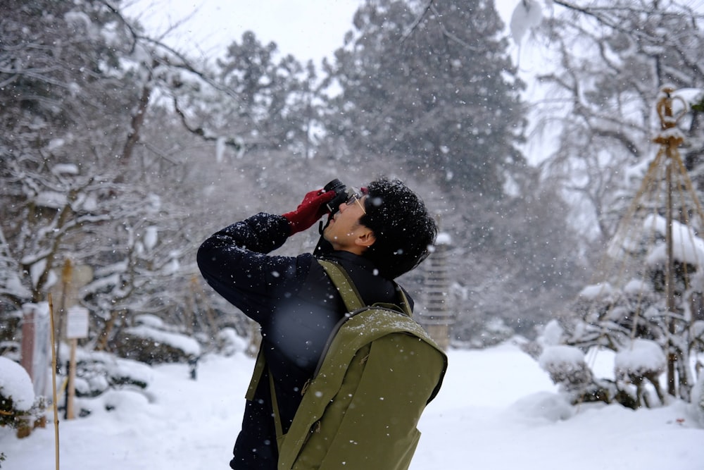 a man standing in the snow looking through a pair of binoculars