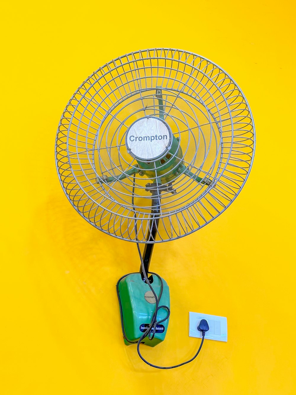 a metal fan sitting on top of a yellow wall