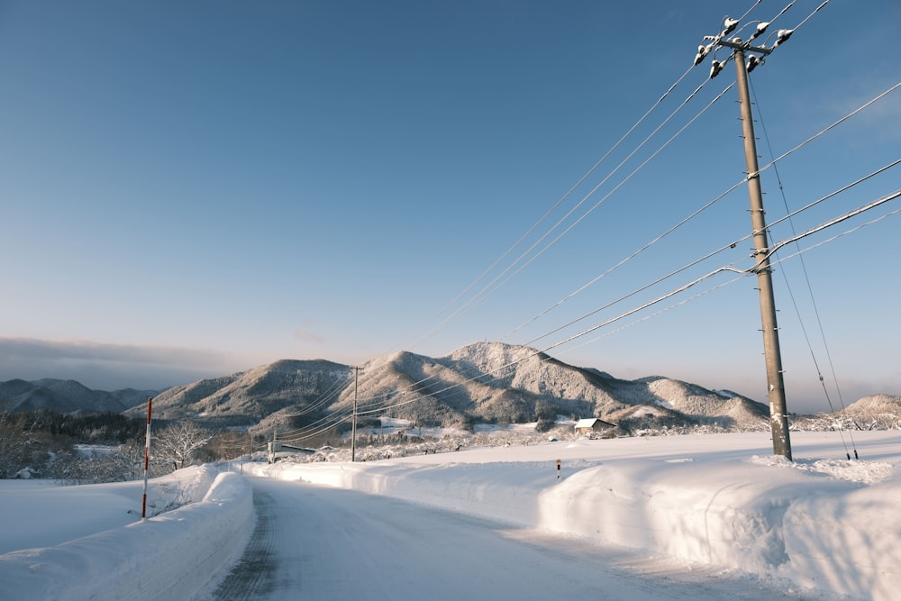 a snow covered road with power lines and mountains in the background