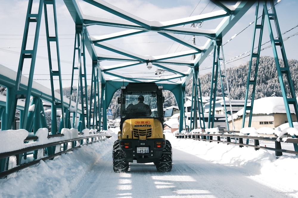 a tractor driving across a bridge in the snow