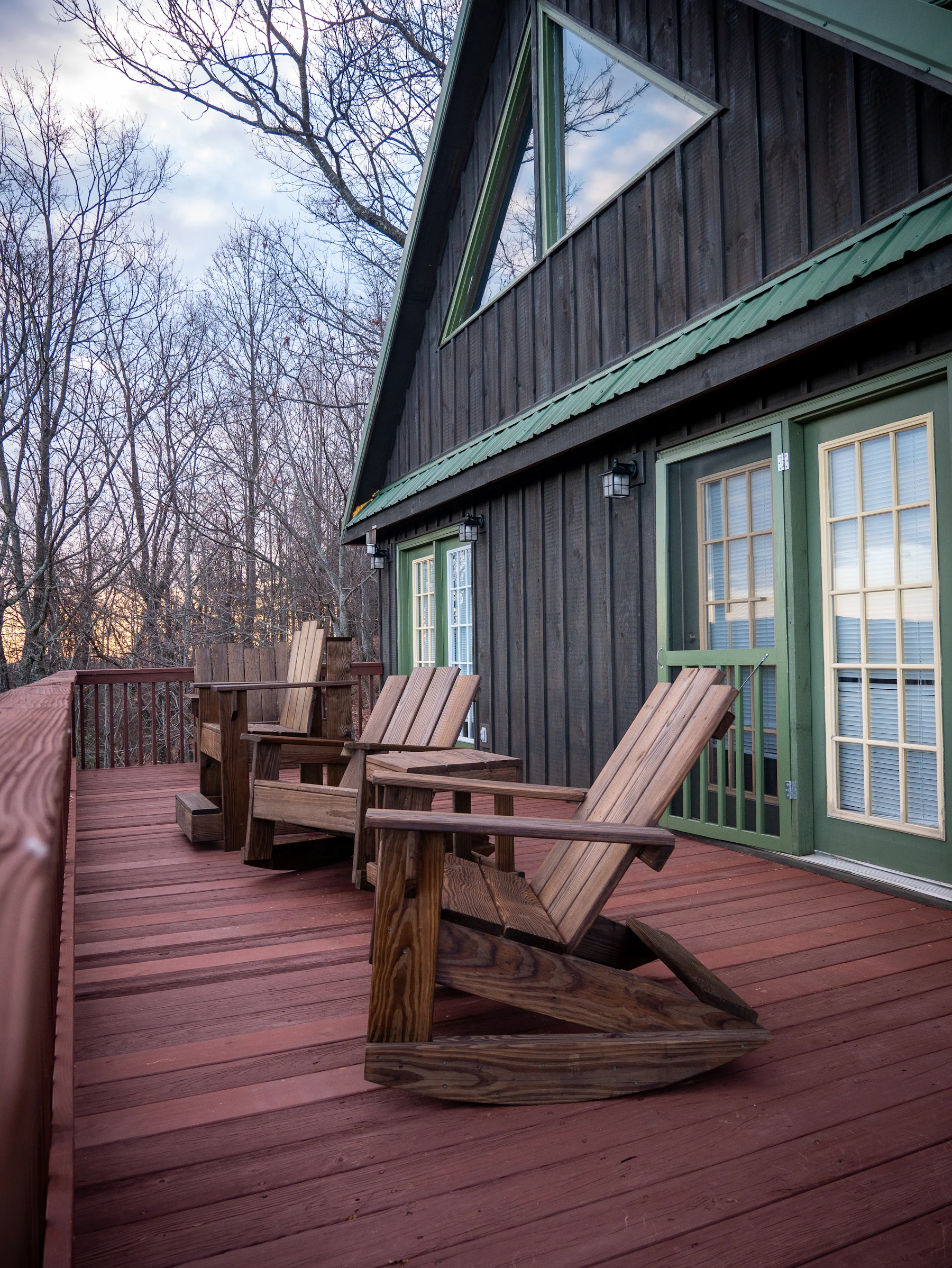 Amber timber deck with heavy wood chairs and railing overlooking a bare forest canopy