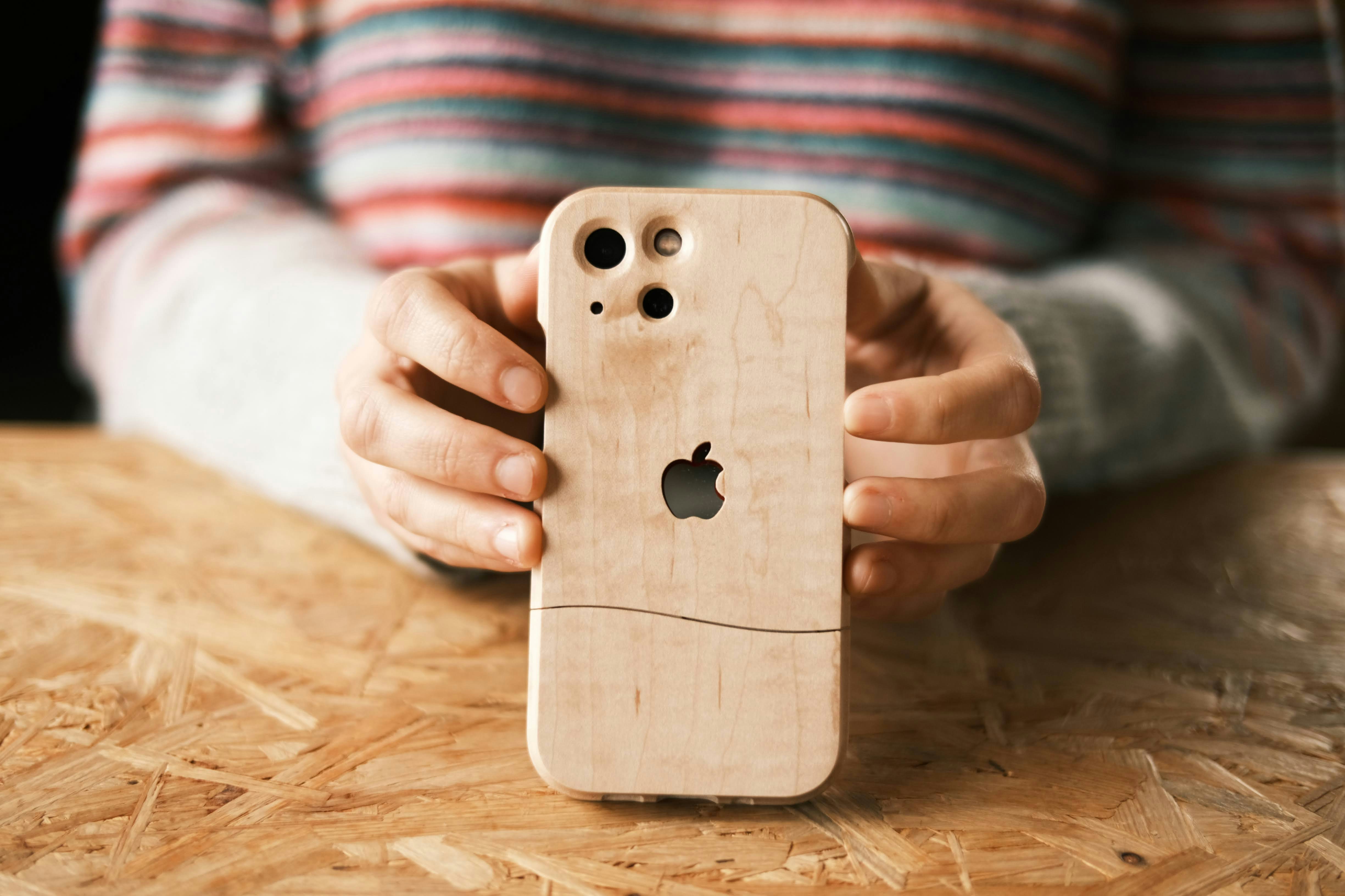 Una persona che tiene una custodia di legno per iPhone su un tavolo