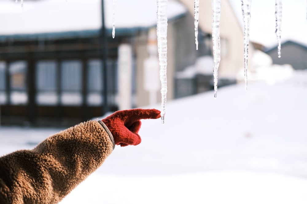 a hand with a red mitt is holding icicles