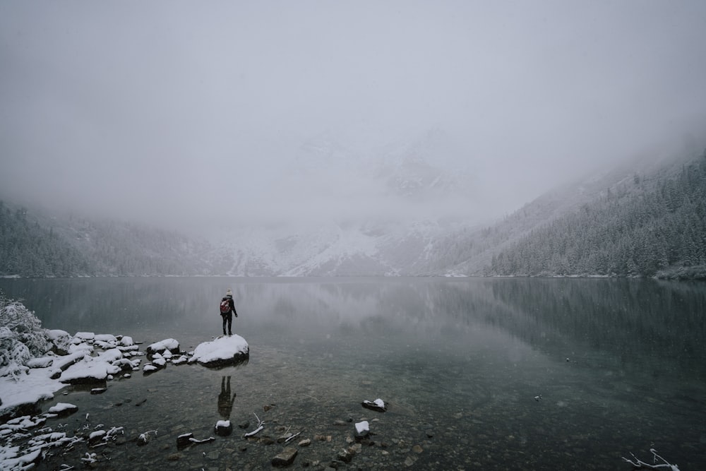 a person standing on the edge of a lake surrounded by mountains