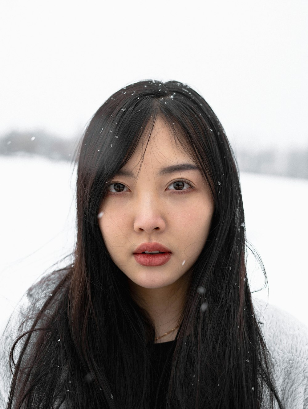 a woman with long black hair standing in the snow