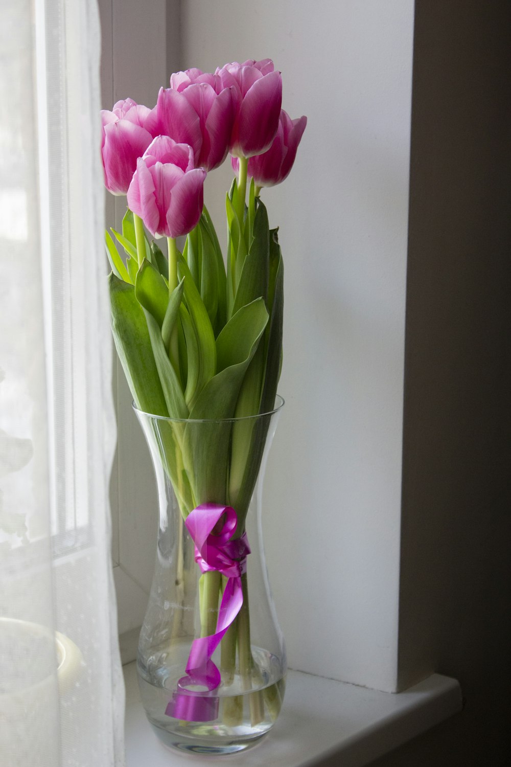 a vase filled with pink tulips sitting on a window sill