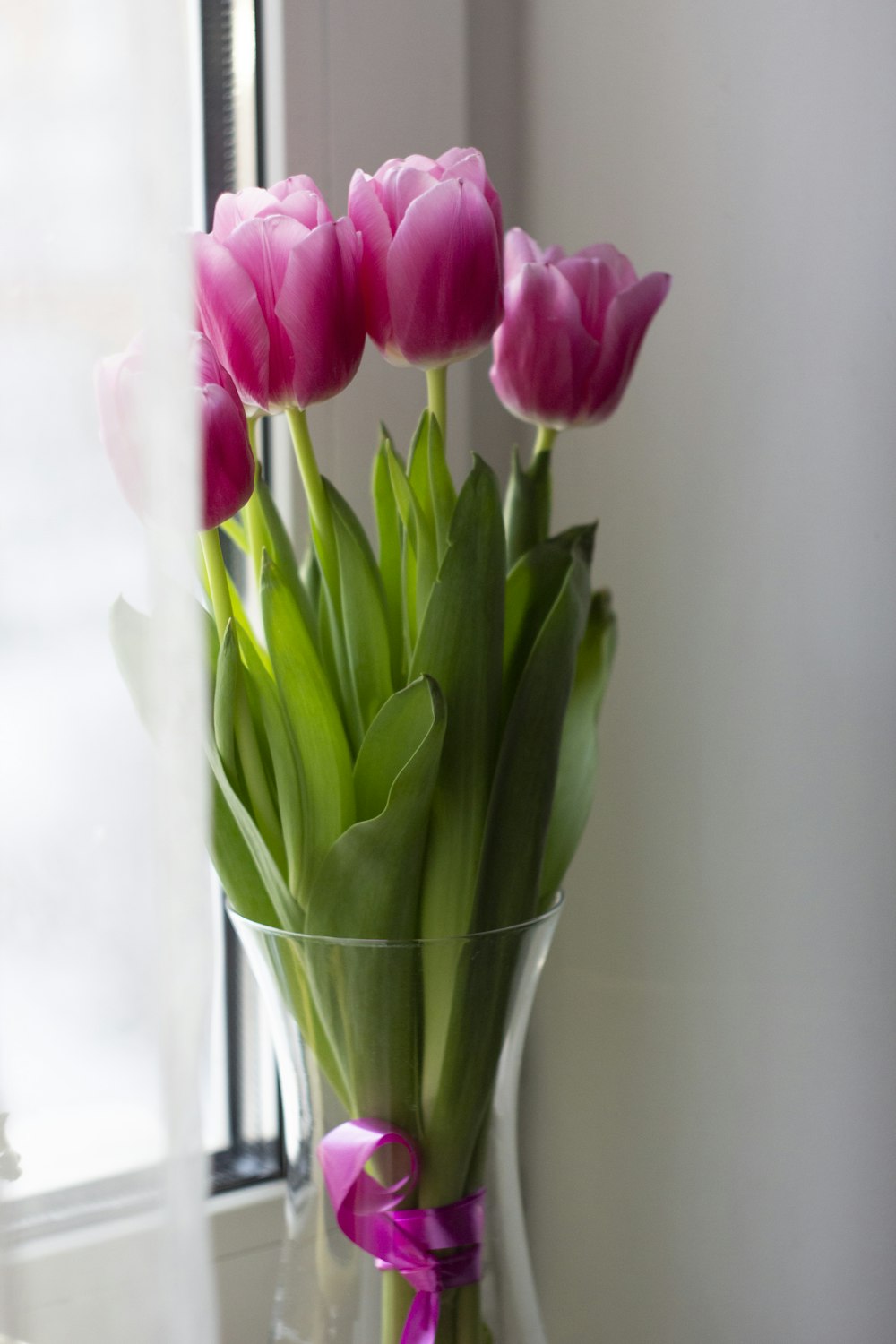 a vase filled with pink tulips next to a window