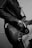 A person wearing a leather jacket plays an electric guitar. The focus is on the hands holding the guitar and the intricate details of the instrument's body, such as the strings, knobs, and pickguard. The image is in black and white, adding a classic and moody feel.