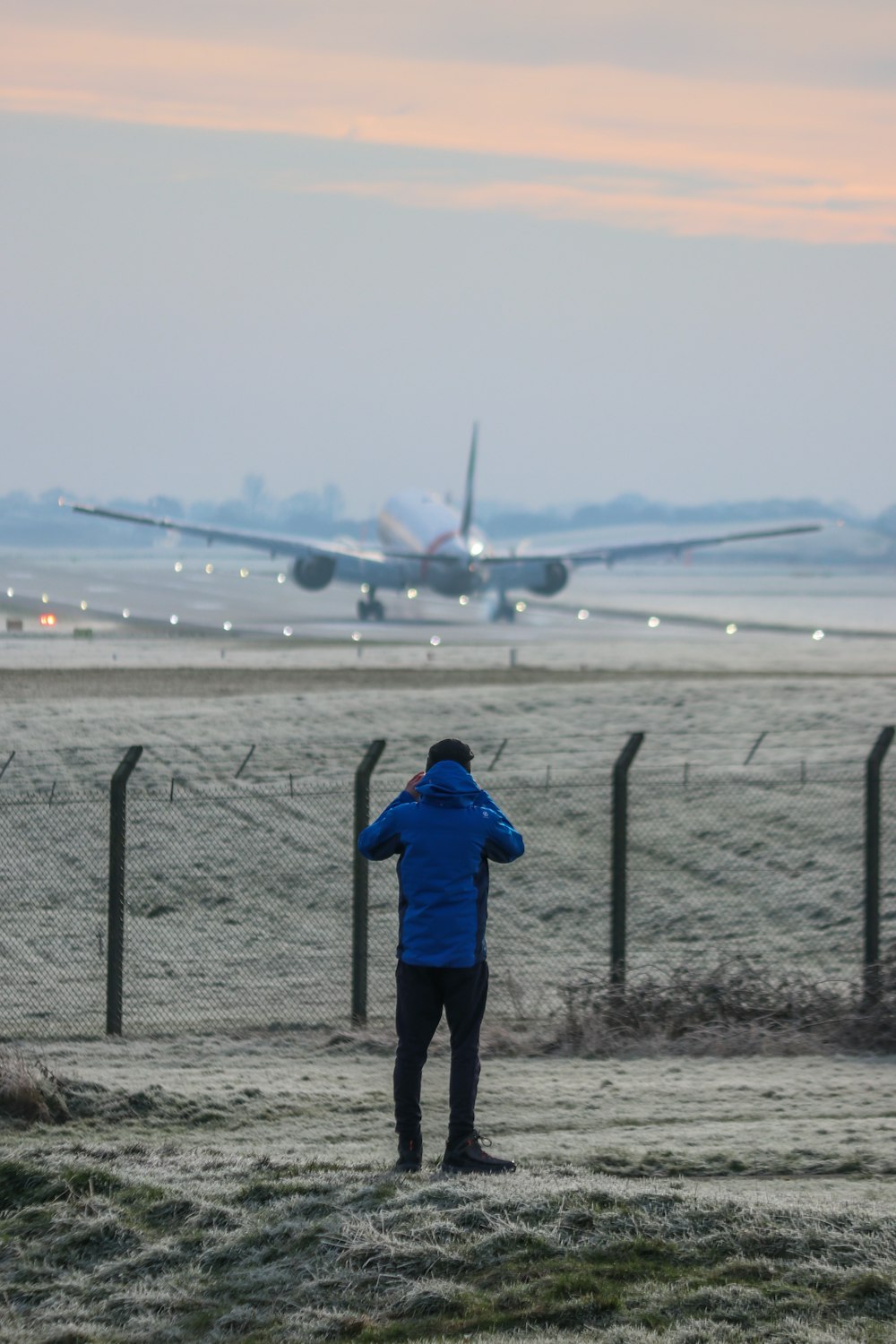 a man standing in front of a fence looking at an airplane