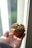 A muffin topped with sunflower seeds rests on a person's open palm. The scene is lit by natural light streaming through a window.
