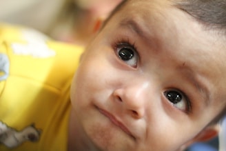 A close-up of an infant's face with expressive eyes and a focused gaze, wearing a yellow garment with small animal designs.