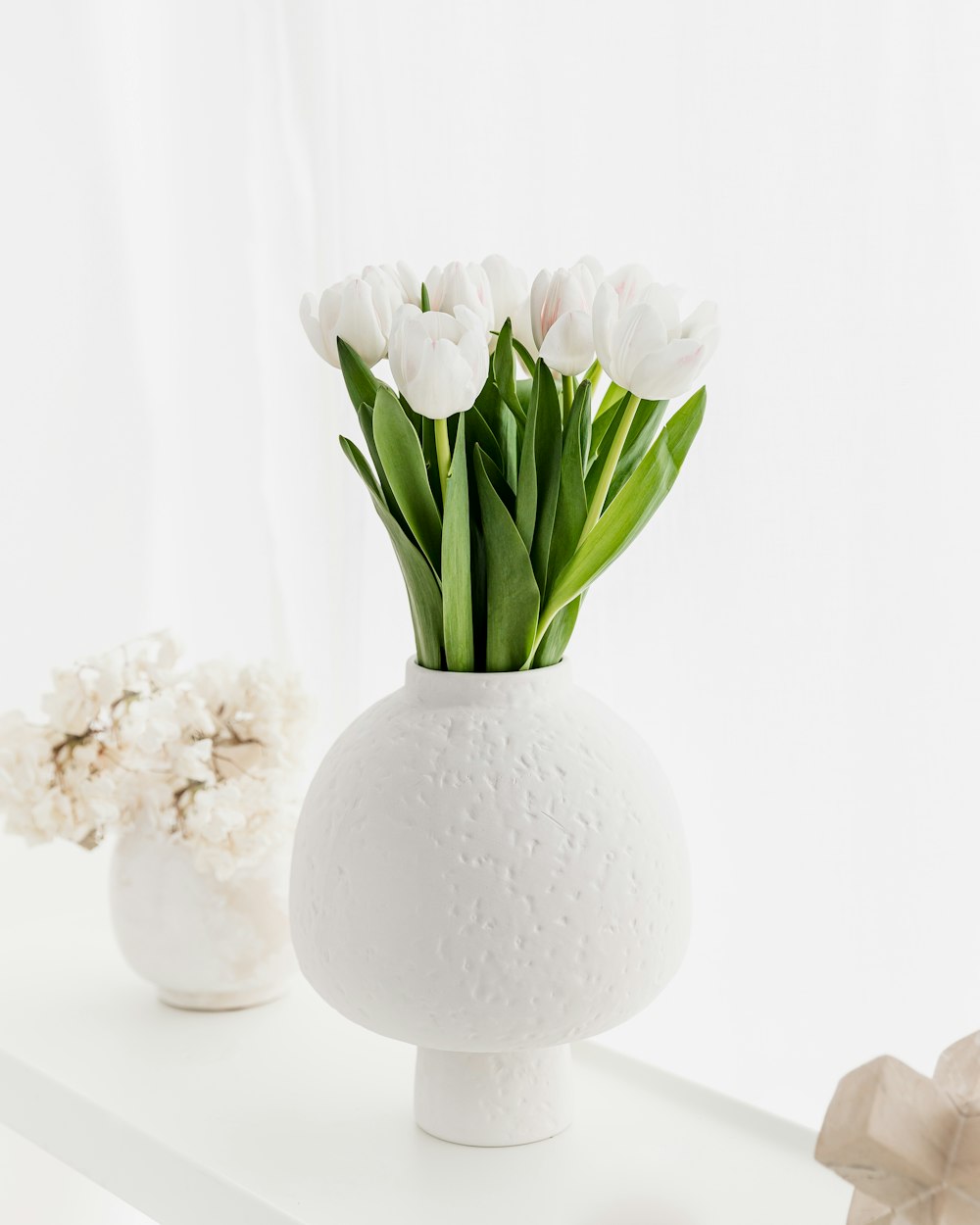 a white vase with flowers in it on a shelf