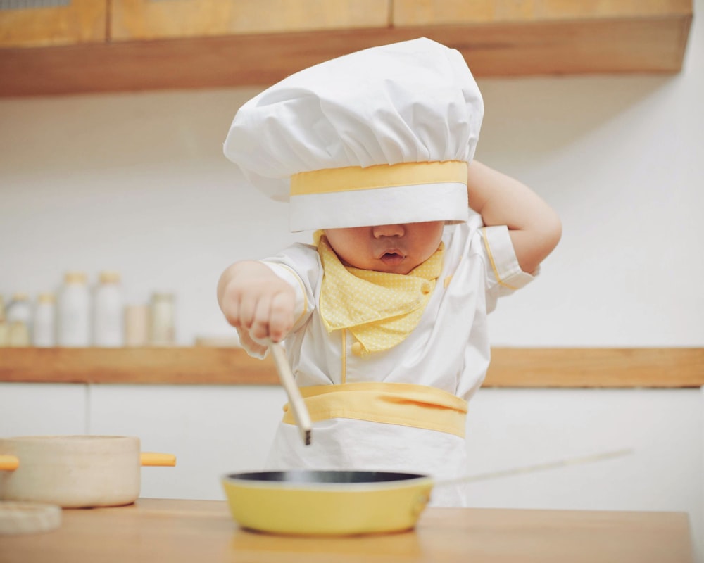 シェフの帽子をかぶってスプーンを持つ幼い子供