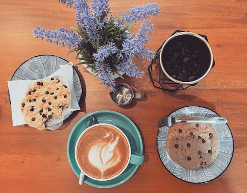 A rustic wooden table displaying vegan gluten-free cookies stacked beside a cup of coffee.