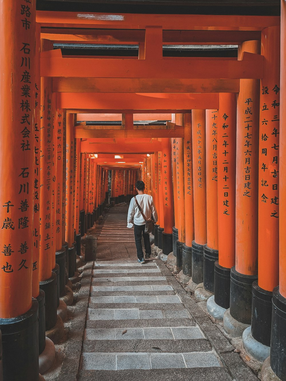 a man walking down a long walkway lined with orange pillars