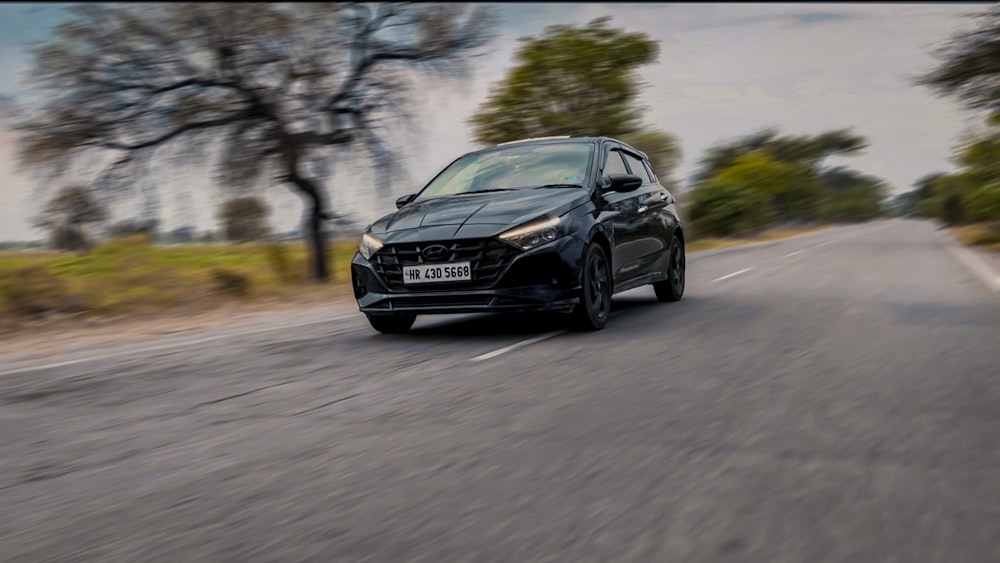 a black car driving down a road next to trees