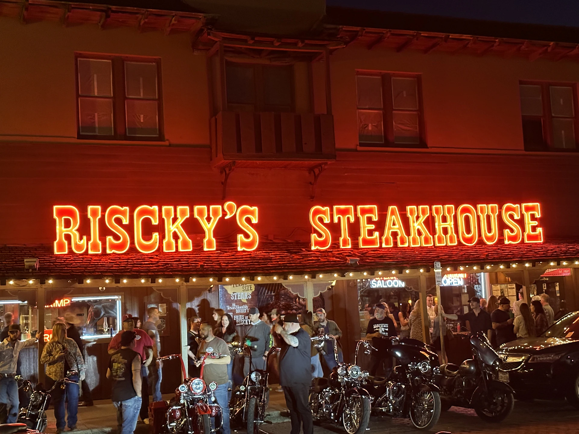 Evening gathering of Road Eagles MC members at Steve's Hangover Bar, with motorcycles parked outside and warm string lights overhead.