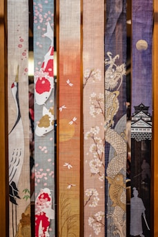 A series of fabric panels with intricate designs including cherry blossoms, koi fish, a crane, a dragon, and a traditional Japanese castle silhouette. The panels display a progression of colors from light to dark, with the use of textile art to portray various traditional Japanese motifs.