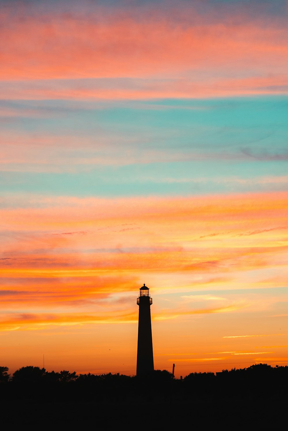 a lighthouse is silhouetted against a colorful sky