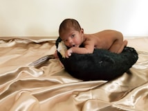 A baby lying on a soft black cushion, surrounded by a luxurious, silky golden fabric.