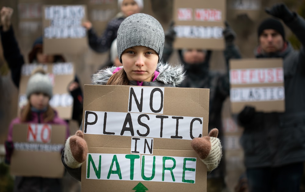 a girl holding a sign that says no plastic in nature