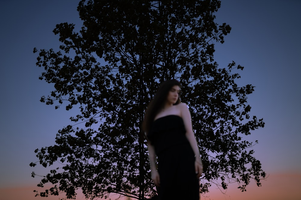 a woman in a black dress standing in front of a tree