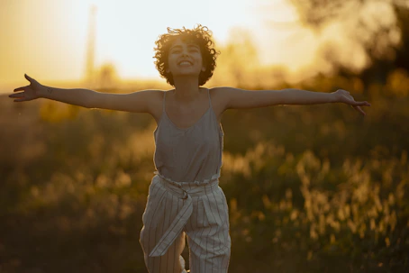 Une femme souriante les bras ouverts dans la lumière semble heureuse.