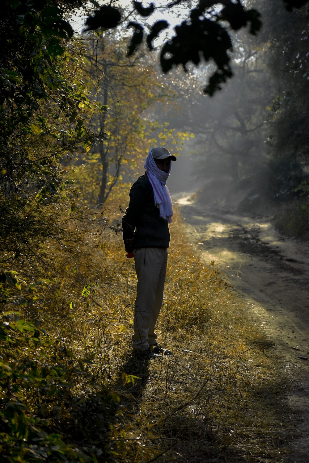 a man standing on a dirt road in the woods