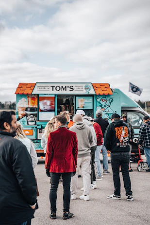 A vibrant orange and white coffee truck parked on a city street with customers enjoying their drinks.