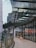 A modern urban setting with a curved glass facade reflecting surrounding buildings. A person wearing shorts and a backpack walks along a tiled pathway adjacent to the glass wall. The architecture features a combination of metal and glass materials, showcasing a contemporary design.