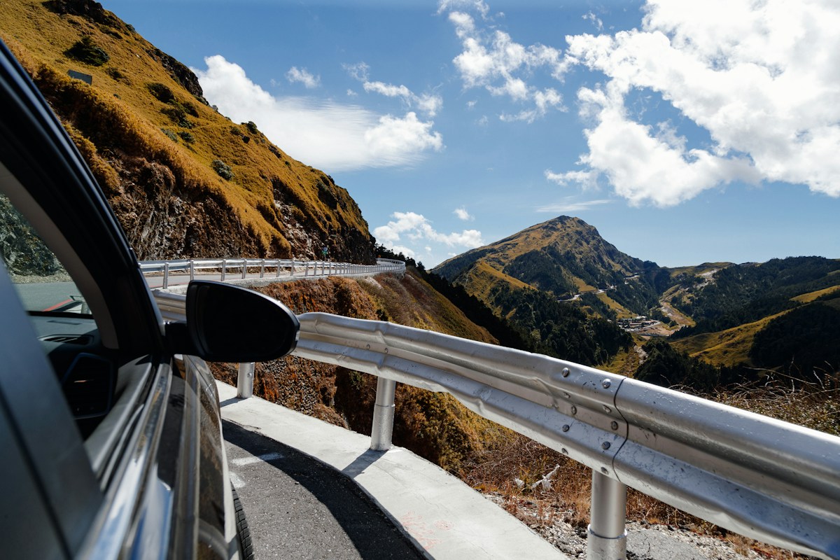 Mountain road on Hehuanshan seen from a car window, with guardrail, ridges and blue sky