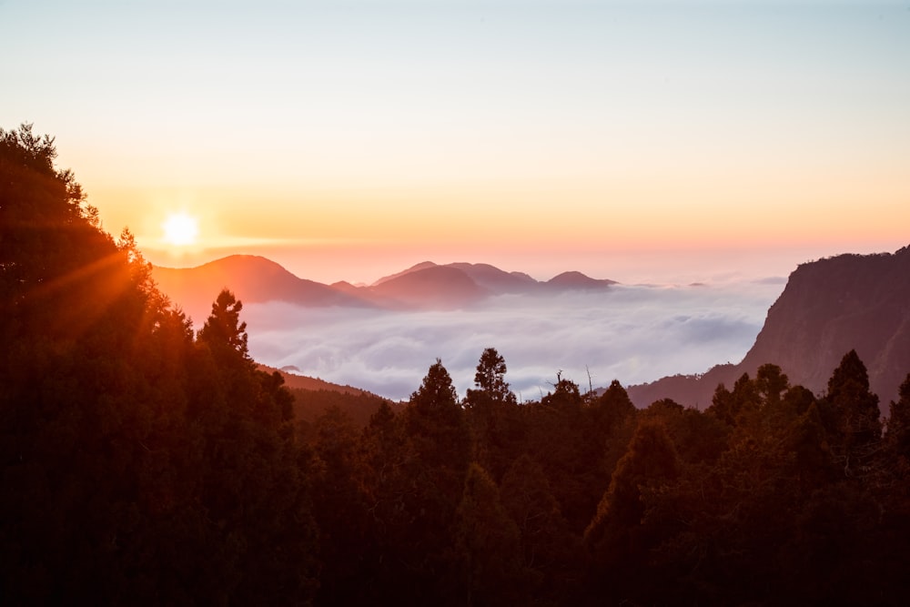 the sun is setting over the clouds in the mountains