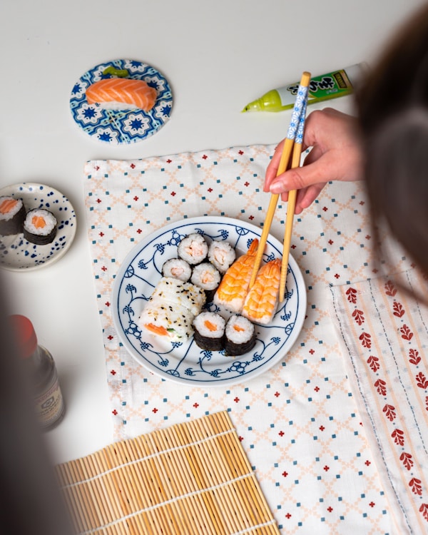 A person holding chopsticks over a plate of sushi