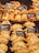 An assortment of baked pastries and empanadas on display with labels indicating different types and prices. The pastries are neatly arranged in rows, showcasing various fillings and crusts. The warm lighting emphasizes the golden-brown color of the baked goods.