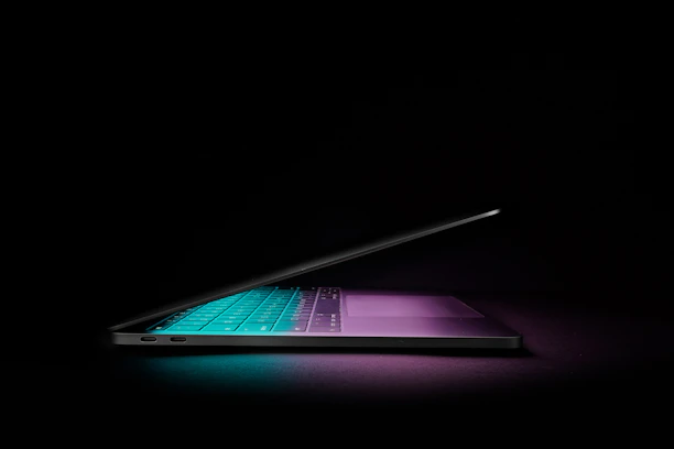 A sleek neon-lit laptop glowing against a dark blue and black gradient background.