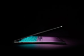 Close-up of a sleek modern laptop with a glowing neon keyboard on a dark desk
