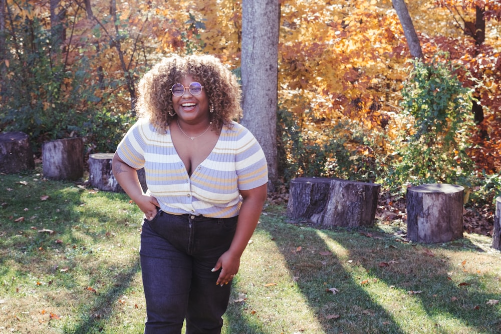 a woman standing in the grass in front of some trees