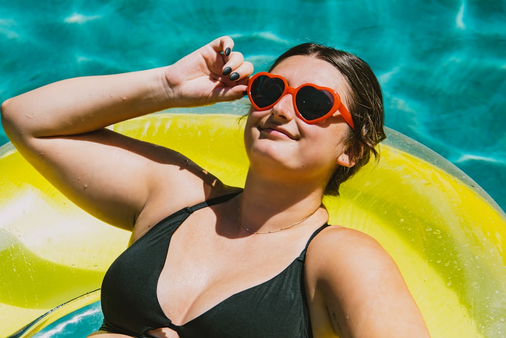 a woman in a black bikini and red sunglasses laying on a yellow raft