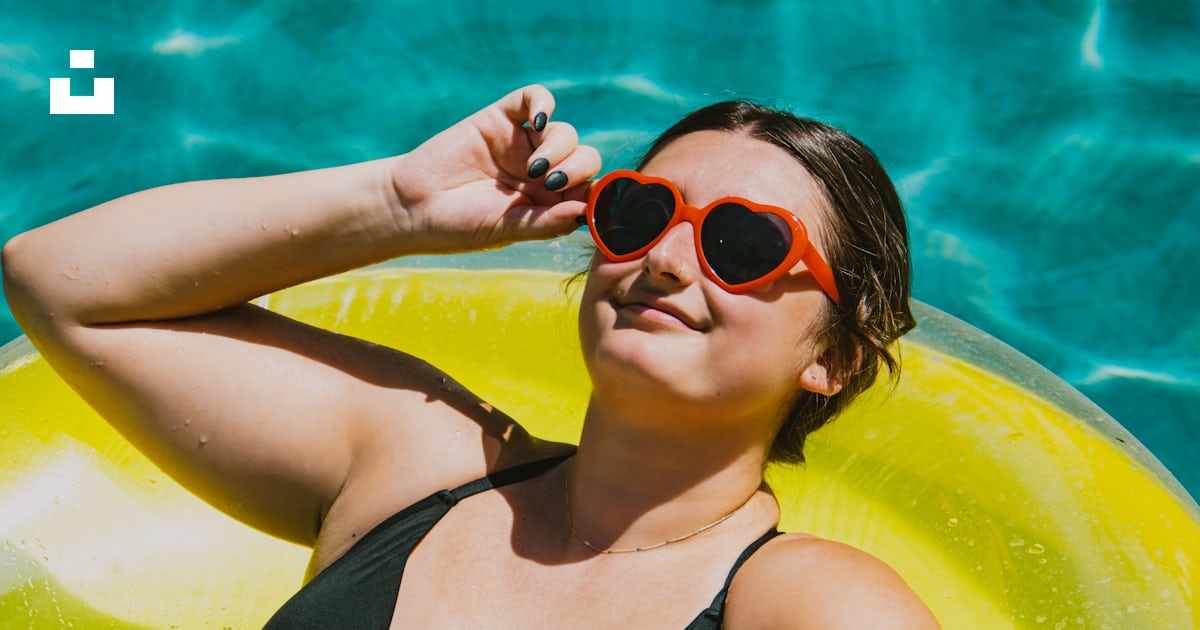 A woman in a black bikini and red sunglasses laying on a yellow raft ...