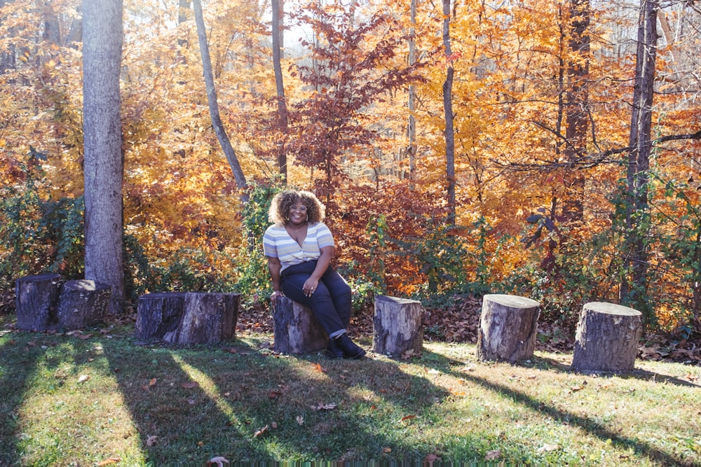 a woman sitting on a tree stump in a forest