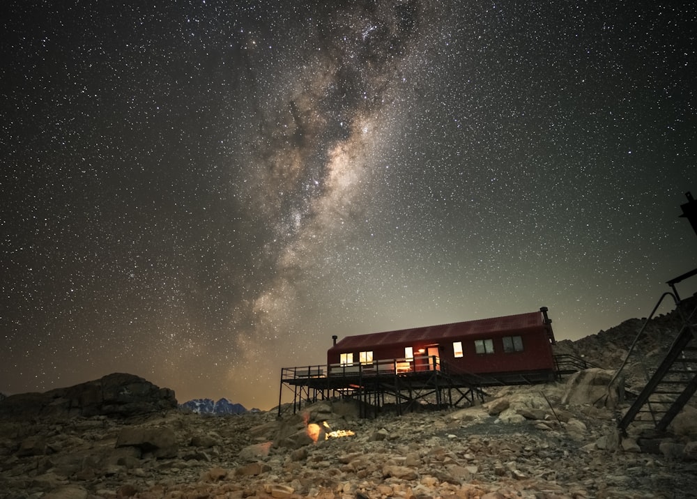 a red cabin sitting on top of a rocky hillside under a night sky filled with