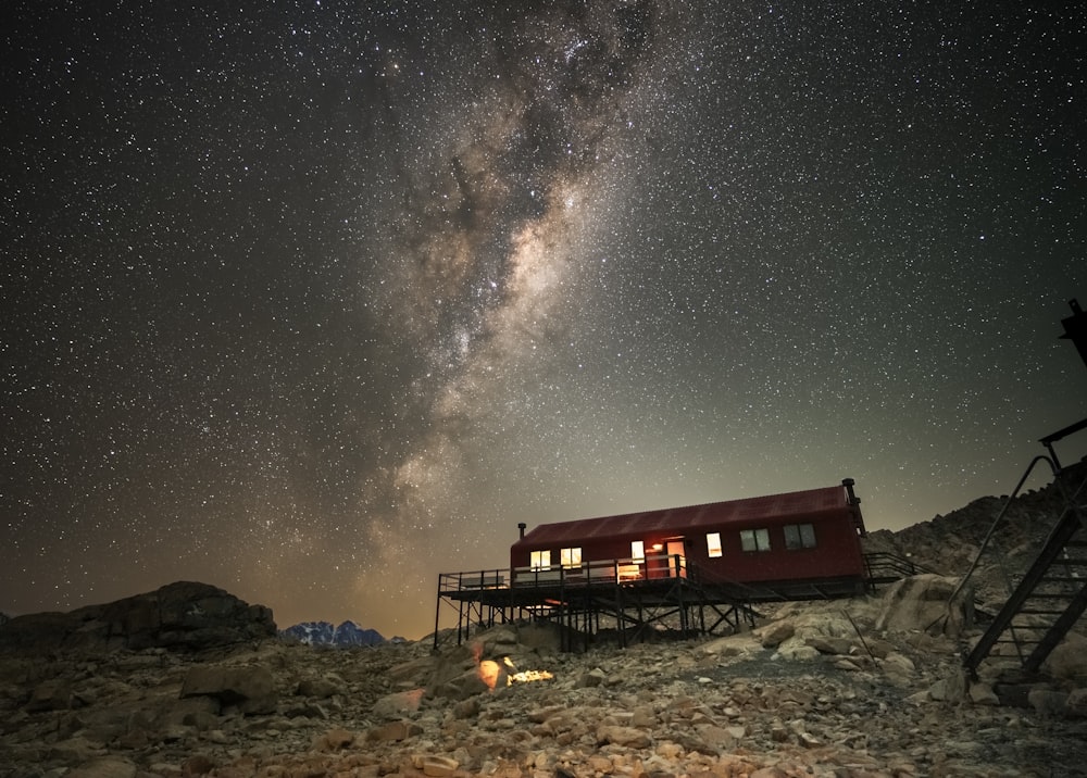 Una cabaña roja sentada en la cima de una ladera rocosa bajo un cielo nocturno lleno de