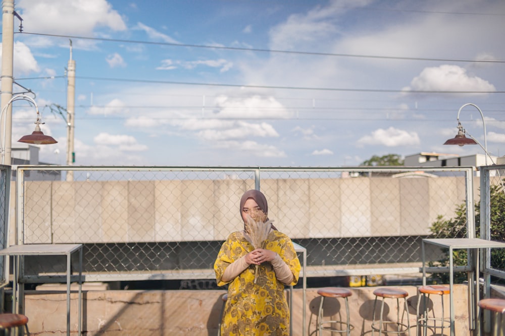 a woman in a yellow dress standing in front of a fence