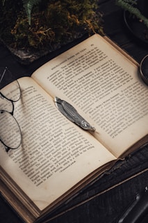 An open vintage book with yellowed pages and a delicate pair of reading glasses resting on top.