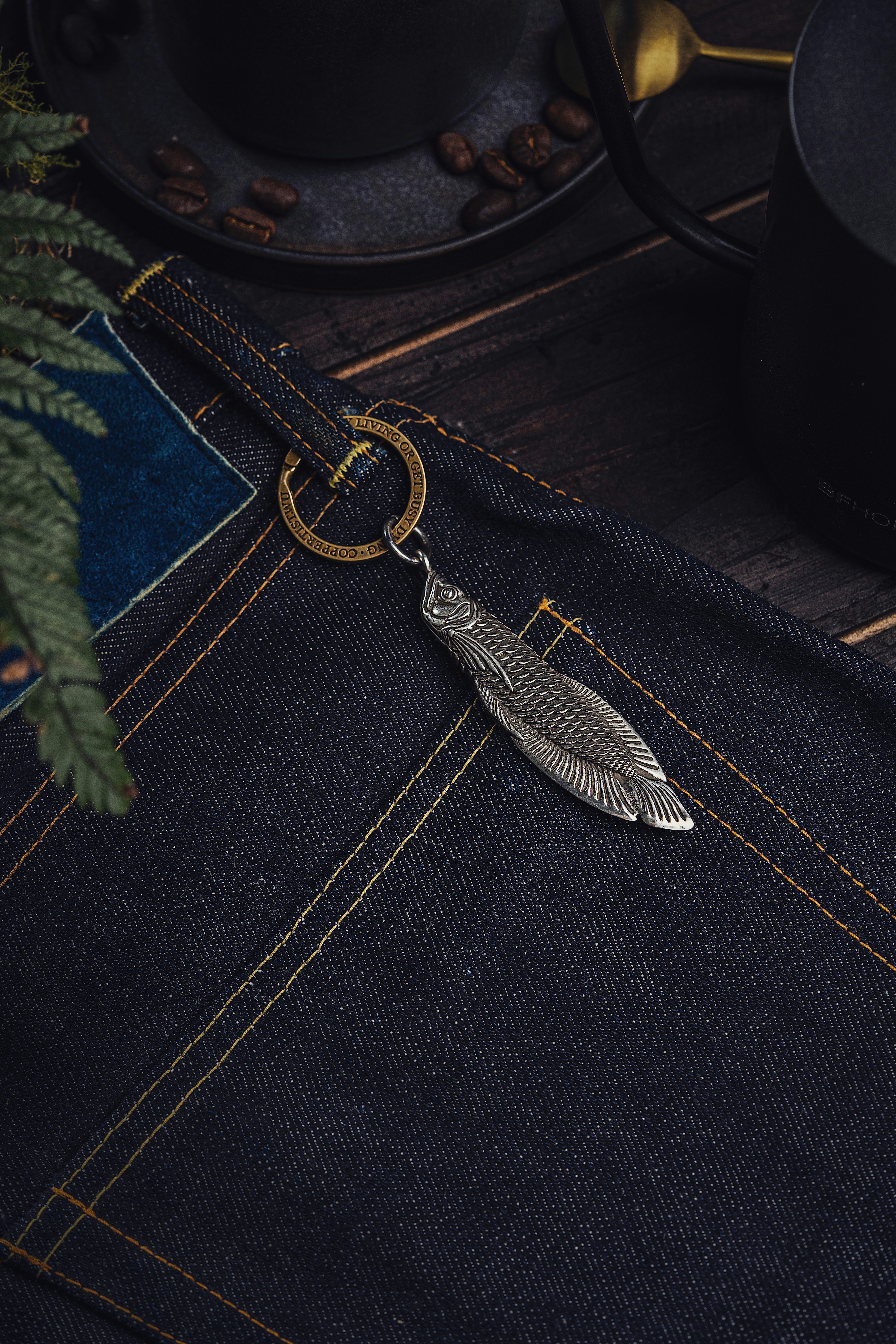 A silver feather keychain sitting on a pair of jeans photo – Free Pants ...