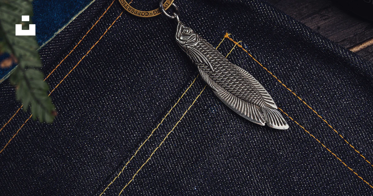 A silver feather keychain sitting on a pair of jeans photo – Free Pants ...