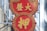 A vibrant red and gold sign with Chinese characters is mounted on the side of a building. The sign features a double circular design with geometric patterns around the edges.