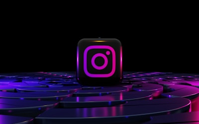 A glowing Instagram logo on a black cube is placed on a futuristic, neon-lit surface with swirling purple and blue patterns. The background is entirely black, enhancing the vibrant glow of the neon colors.