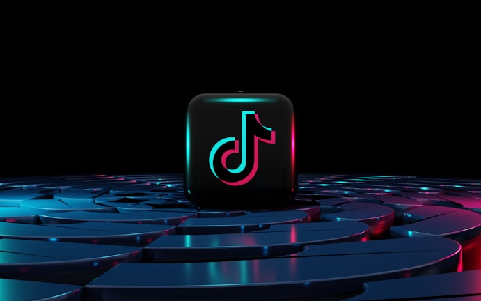 A black block with a neon TikTok logo in the center, surrounded by a futuristic, glowing platform with shades of blue and pink, set against a dark background.